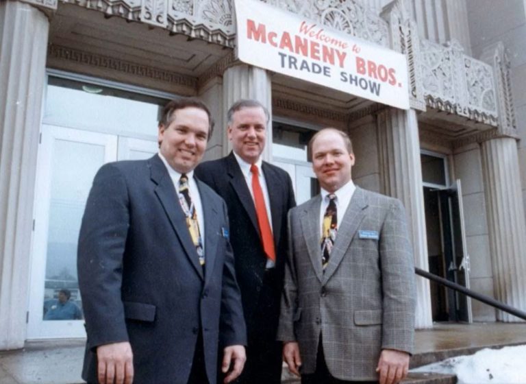 3 brothers standing in front of McAneny Brothers Trade Show banner